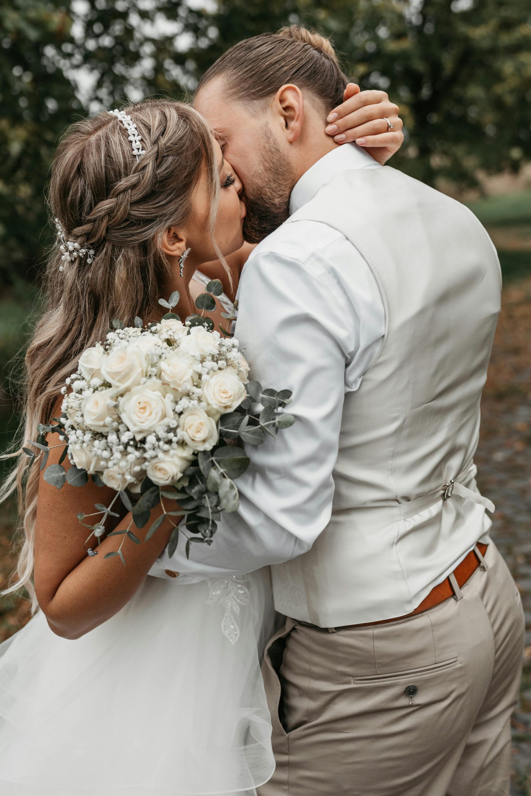 A bride and groom share a romantic kiss outdoors, showcasing elegance.